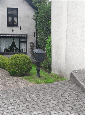 Foto van een stuk bestrating, een afrit en een huis en tuin op de achtergrond.