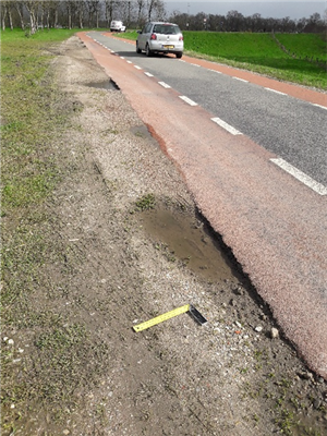 Foto van een zanderige berm naast een asfaltweg.
